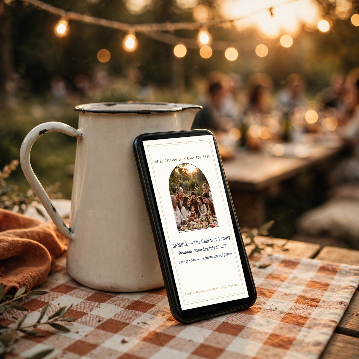 Hand holding a phone showing a family reunion announcement card with the family's group photo, generations gathered in a park pavilion behind them