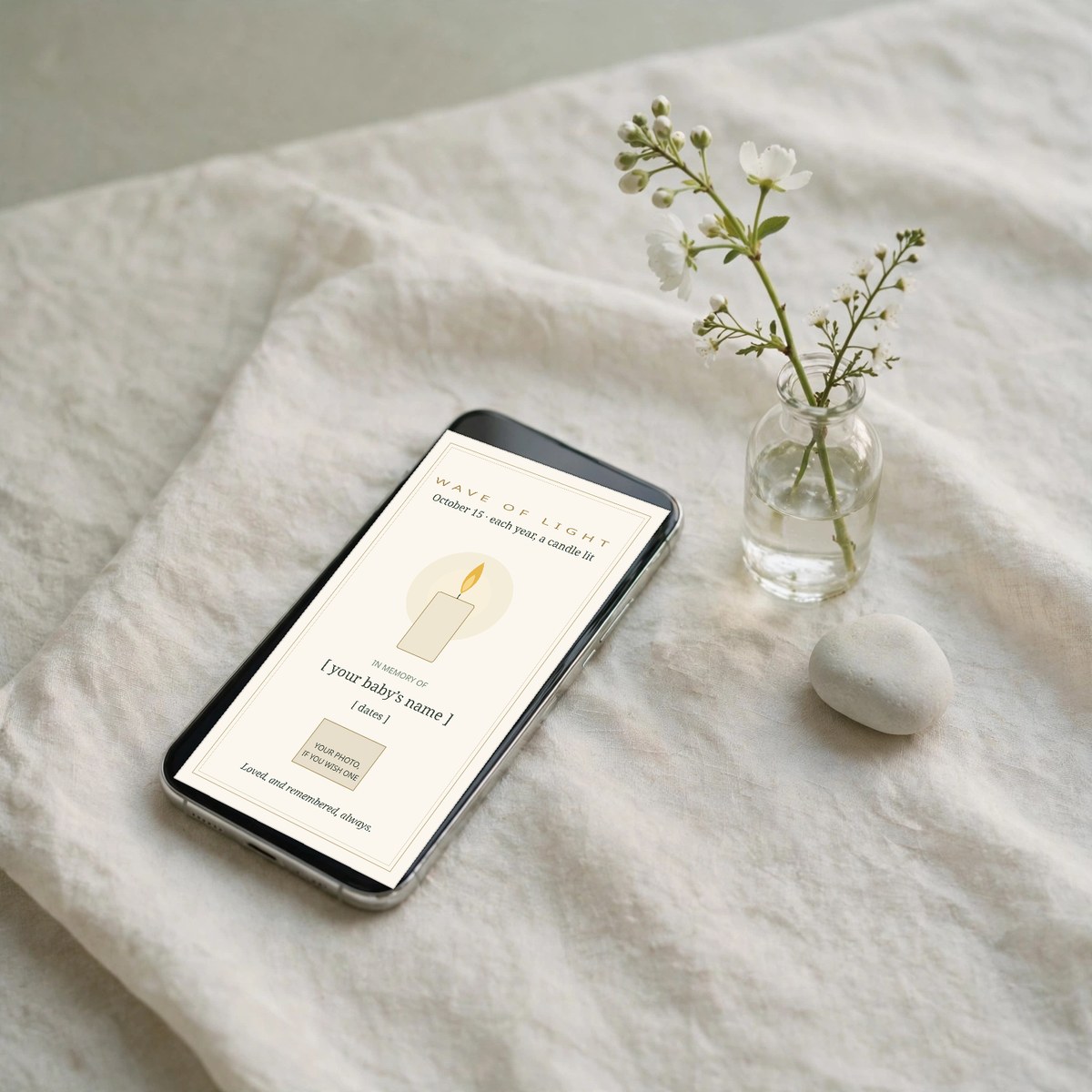 Hand holding a phone showing a Wave of Light remembrance keepsake card with a softly lit candle and placeholder lines for a baby's name and dates, on a quiet wooden table with a lit candle beside it