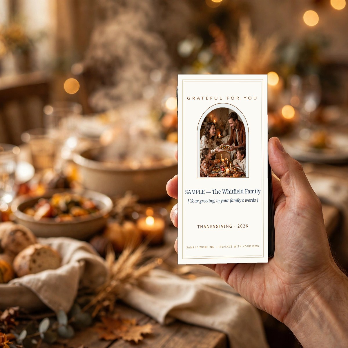 Hand holding a phone showing a Thanksgiving greeting card with the family's own photo and greeting, the family's long dinner table set behind them